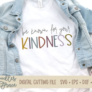Peut inclure: Un t-shirt blanc avec le texte "be known for your KINDNESS" en lettres colorées. Le texte est écrit à la main. Le t-shirt est posé sur une veste en jean bleu clair et un fond en toile blanche.