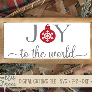 May include: A white wooden sign with the text "JOY to the world" in gray lettering. A red Christmas ornament with a snowflake is centered between the words "JOY".