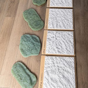 May include: Four square white textured panels with DFA branding on the side, arranged in a vertical column. To the left of each panel is an irregularly shaped, light green, textured object of varying size, resembling a natural stone or rock form.