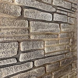 Könnte beinhalten: Nahaufnahme einer strukturierten Wand mit einem Steinziegeldesign. Die Ziegel sind rechteckig und unterschiedlich groß, mit einer rauen, unebenen Oberfläche. Die Farbpalette ist neutral und weist Grautöne, Beige und Braun auf, wodurch eine rustikale Ästhetik entsteht.