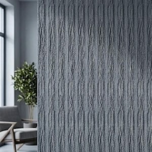 May include: A textured, vertical panel in shades of gray, resembling tree bark. The panel is part of an interior design, with a glimpse of a chair and a plant in the background. The surface has a rough, organic appearance.