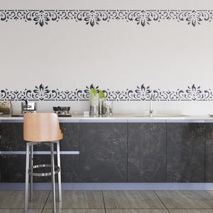 Op de afbeelding: Een moderne keuken met donkere kasten en een wit aanrechtblad. De muur heeft een decoratieve bloemenrand in een donkerblauwe kleur. Een lichtbruine barkruk staat voor het aanrecht en de vloer is betegeld.