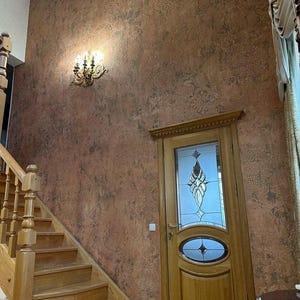 Puede incluir: Toma interior que muestra una escalera de madera con una balaustrada decorativa, que conduce a una pared con papel pintado marrón rojizo estampado. También se ve una puerta de madera con paneles de vidrio y una lámpara de araña decorativa.