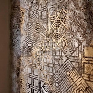 May include: Textured wall art with a geometric pattern in gold and gray. The design features squares, circles, and diamond shapes, creating a layered effect. The artwork has a vintage, weathered appearance.