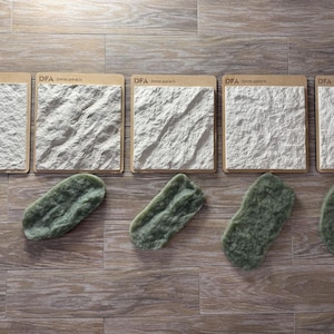 May include: An image showing stone samples and decorative rocks. Five square samples with textured white surfaces are arranged above five green, irregularly shaped rocks. The samples are mounted on cardboard with text. The rocks vary in size and shape.