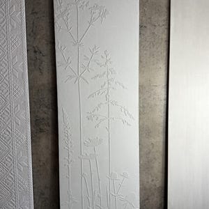 May include: White rectangular panel with an embossed botanical design featuring various plants and flowers. The panel has a textured surface and is flanked by other white panels with decorative patterns.