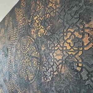 Peut inclure: Œuvre d'art murale texturée avec un schéma de couleurs gris foncé et or. L'œuvre présente des motifs géométriques et circulaires répétés. La surface a une texture rugueuse en relief, créant une sensation de profondeur et d'intérêt visuel. Les accents dorés ajoutent une touche de chaleur.