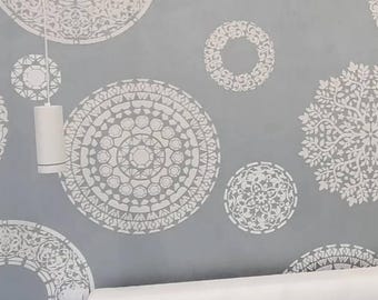 May include: A gray wall featuring multiple white circular stenciled patterns with intricate geometric and floral designs. A white cylindrical pendant light hangs on the left side, and a white tufted headboard is positioned at the bottom.