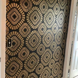 Peut inclure: Un mur recouvert de papier peint présentant un motif répétitif de formes en losange arrondies dorées sur un fond noir uni. Le design se compose de lignes rayonnantes à l'intérieur de chaque forme, créant un aspect texturé sur la surface.