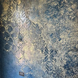 Könnte beinhalten: Eine strukturierte Wandoberfläche mit einer tiefblauen Grundierung und abgenutzten Goldakzenten. Ein sich wiederholendes Muster aus stilisierten Blättern und geometrischen Formen ist auf der linken Seite eingeprägt und bildet einen Kontrast.