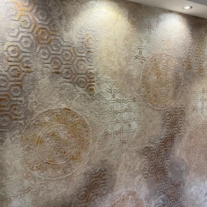 May include: Textured wall with a beige and brown color scheme. The wall features geometric and circular patterns, with a mix of hexagonal and floral designs. The lighting highlights the raised textures, creating a sense of depth and visual interest.