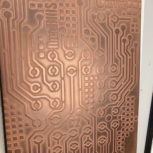 Peut inclure: Une carte de circuit imprimé de couleur cuivre avec des chemins gravés, des carrés et des éléments circulaires. La carte comporte le texte "C BOARD KSFV712", "SOKIBIO" et les étiquettes "C2" et "C3". Le design ressemble à un schéma électronique complexe.