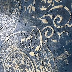 May include: Close-up of a textured abstract artwork with a dark blue background. The design features raised, cream-coloured floral and circular patterns. The artwork has a distressed, aged appearance, with visible texture and colour variations.