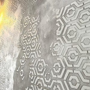 Könnte beinhalten: Eine strukturierte graue Wand mit weißen geometrischen Mustern. Die Muster umfassen sich wiederholende Formen wie Sechsecke und andere abstrakte Designs. Die Wand hat ein raues, industrielles Aussehen, mit einer netzartigen Textur, die in einigen Bereichen sichtbar ist.