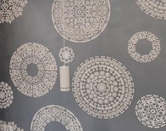May include: A gray wall decorated with multiple white circular mandala-style stenciled patterns of varying sizes. A white cylindrical pendant light hangs from the ceiling in front of the wall, and a white headboard is visible at the bottom.