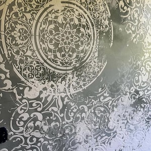 May include: A textured wall with a repeating pattern of white floral and geometric designs on a gray background. The design includes circular and swirling elements, creating a decorative and ornate appearance. The wall has a layered, dimensional effect.