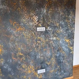 Può includere: Arte murale strutturato con una combinazione di colori grigio scuro, oro e argento. Il design presenta motivi circolari e geometrici, con un aspetto invecchiato e usurato. Sono visibili prese elettriche sulla parete.