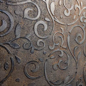 May include: Close-up of a textured wall with a repeating pattern of swirling, stylized floral and leaf designs. The raised design is a dark gray color, contrasting with the mottled brown background. The overall effect is a vintage, decorative style.