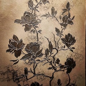 May include: A rectangular wall art piece featuring a raised, dark brown relief of magnolia flowers and branches set against a textured, metallic gold background. The floral design displays multiple blooming flowers and buds in a vertical arrangement.