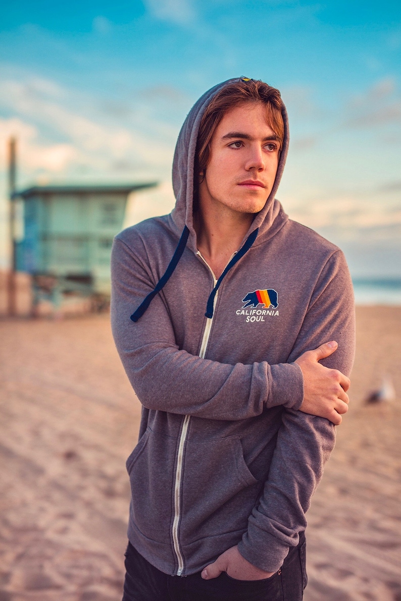 May include: A grey zip-up hoodie with a navy blue drawstring and a graphic of a bear with the text "California Soul".