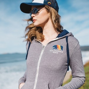 May include: A grey zip-up hoodie with a navy blue hood and a California Soul logo featuring a bear with a rainbow design.