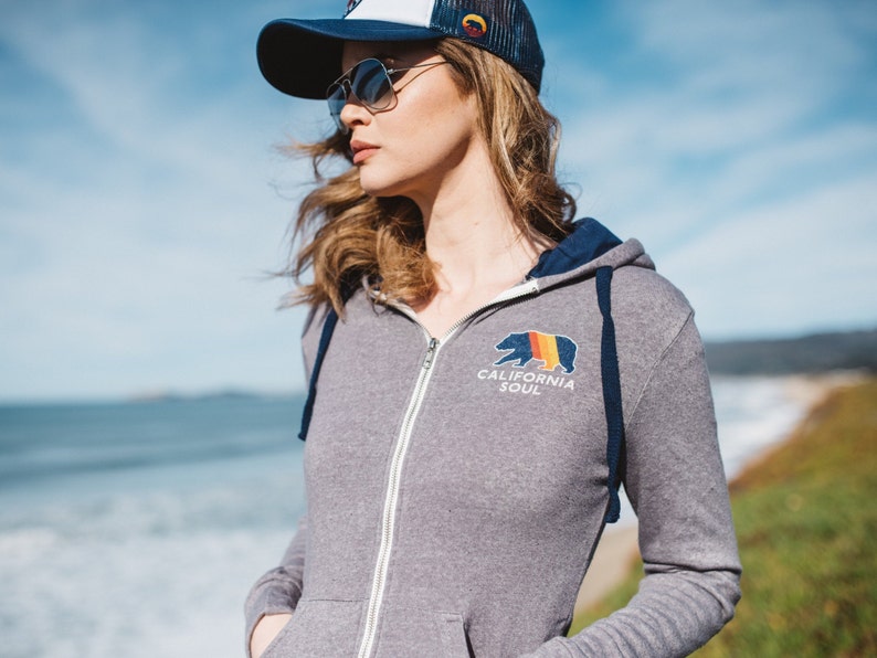 May include: A grey zip-up hoodie with a navy blue hood and a California Soul logo featuring a bear with a rainbow design.