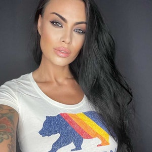 May include: A white t-shirt with a blue bear graphic and a rainbow stripe design. The text "CALIFORNIA SOUL" is printed below the bear.