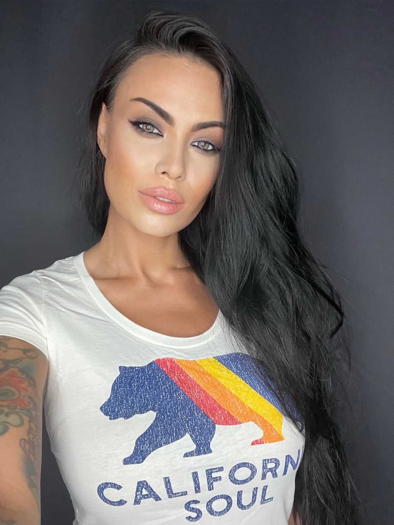 May include: A white t-shirt with a blue bear graphic and a rainbow stripe design. The text "CALIFORNIA SOUL" is printed below the bear.