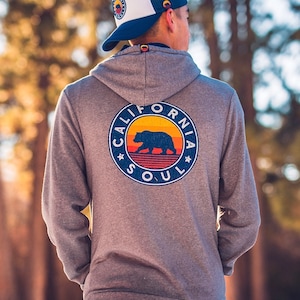 May include: A grey hooded sweatshirt with a vintage-style graphic on the back. The graphic features a bear silhouette with a sunset and the text "California Soul".