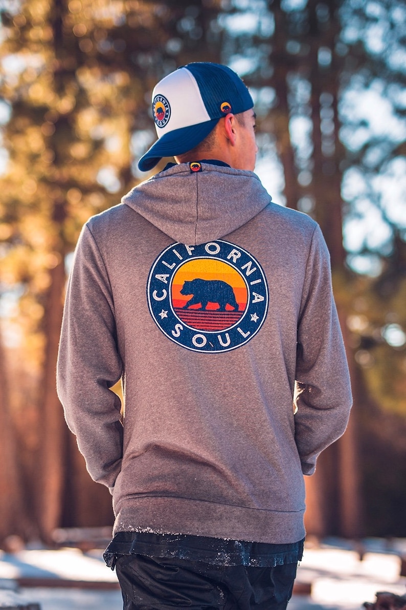 May include: A grey hooded sweatshirt with a vintage-style graphic on the back. The graphic features a bear silhouette with a sunset and the text "California Soul".