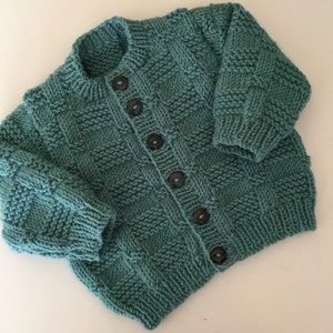 May include: A teal blue knitted cardigan with a button closure. The cardigan has a textured stitch pattern and is made with a soft yarn.