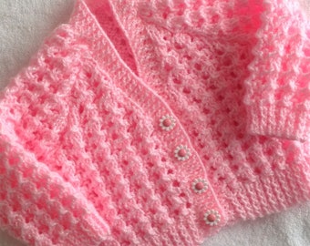 May include: A pink crocheted baby cardigan with white flower buttons.