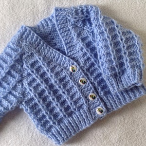 May include: A light blue knitted baby cardigan with a button closure and a waffle stitch pattern.