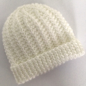 May include: A white knitted beanie hat. The hat is made with a textured stitch pattern.