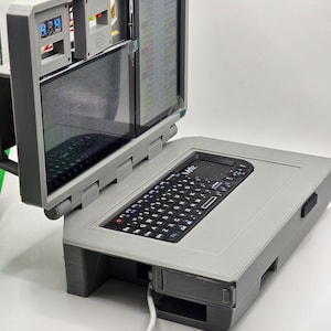 May include: A gray 3D printed laptop with a small keyboard and a screen that is open to reveal a smaller screen with text that reads "PL5 GPIO Layout".