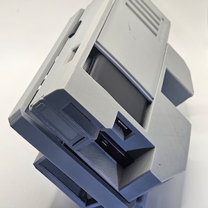 May include: A gray 3D printed case with a black rectangular object inside. The case has a hinged lid and a series of vents on the top.