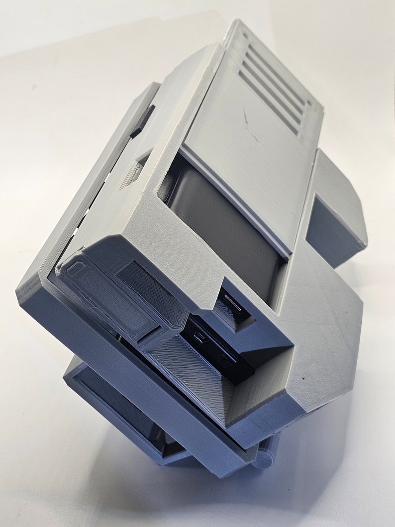 May include: A gray 3D printed case with a black rectangular object inside. The case has a hinged lid and a series of vents on the top.