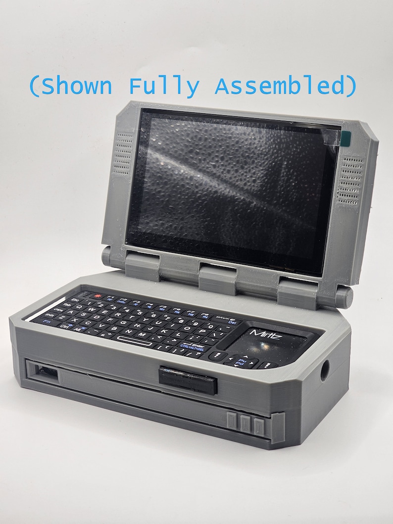 Pu&ograve; includere: Un computer portatile grigio, stampato in 3D, con una tastiera nera, un piccolo schermo e il testo "Mintz" sul davanti. Il computer &egrave; mostrato completamente assemblato.