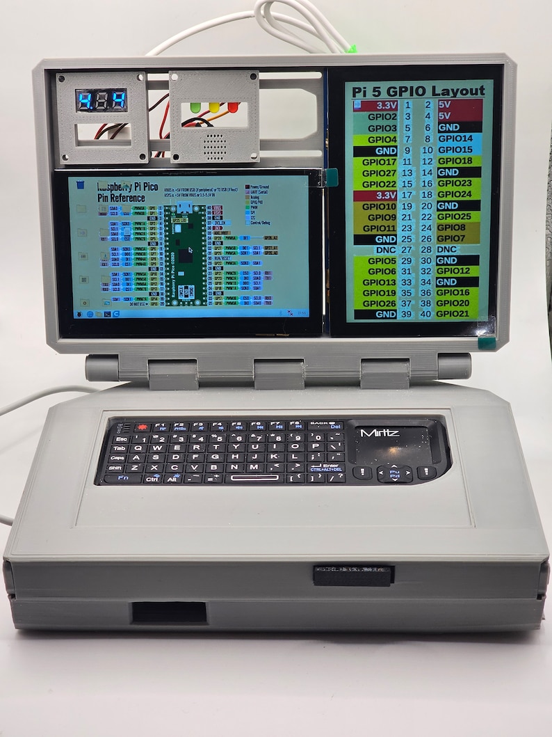 May include: A gray laptop with a black keyboard and a small touchpad labeled "Mirttz". The laptop has a screen that is open and shows a Raspberry Pi Pico Pin Reference diagram and a Pi 5 GPIO Layout diagram. The screen also shows a digital display with the number 8.8.