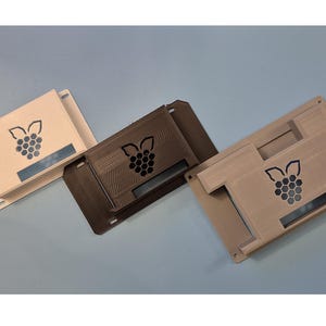 May include: Three 3D printed Raspberry Pi cases in different colors: beige, brown, and a darker beige. Each case has a Raspberry Pi logo on the front.