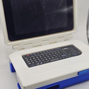 May include: A white and blue portable computer with a black keyboard and a small screen. The computer has the word "Miritz" printed on it.