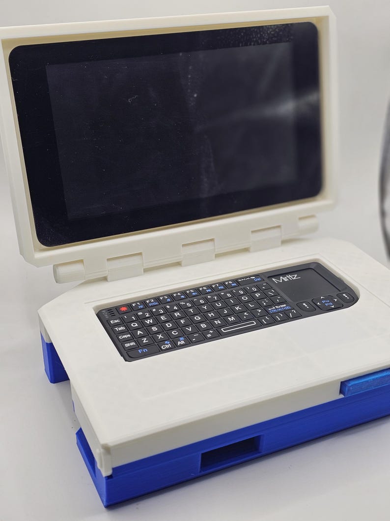 May include: A white and blue portable computer with a black keyboard and a small screen. The computer has the word "Miritz" printed on it.