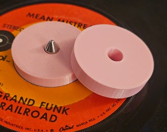 Könnte beinhalten: Zwei hellrosa Schallplattenstabilisatoren auf einer Schallplatte. Einer hat eine silberne, kegelförmige Spindel, der andere ein Loch in der Mitte. Das Plattenetikett ist orange und schwarz mit dem Text "GRAND FUNK RAILROAD".
