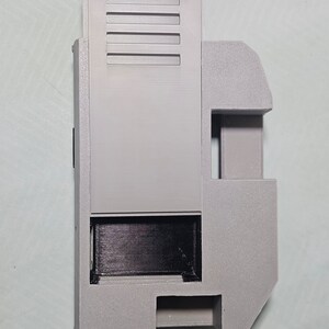 May include: A gray plastic 3D printed case with a rectangular opening and a series of vents on the side.