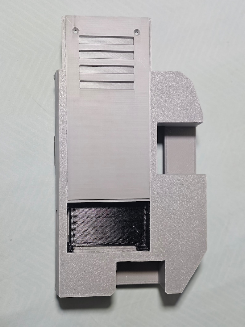 May include: A gray plastic 3D printed case with a rectangular opening and a series of vents on the side.