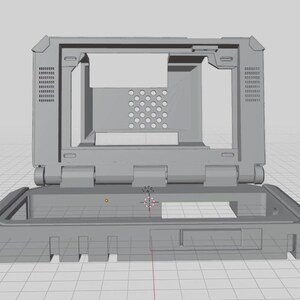 May include: A gray, open-top computer case, likely for a laptop or similar device. The case is rectangular with a hinged top and features various openings and vents. The design appears to be a 3D model or prototype.