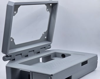 May include: A gray 3D printed case with a hinged lid, designed to hold a small electronic device. The case has several openings for ports and buttons.