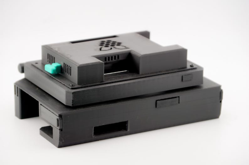 May include: A black Raspberry Pi case with a green button and a black Raspberry Pi logo. The case is stacked on top of another black case.