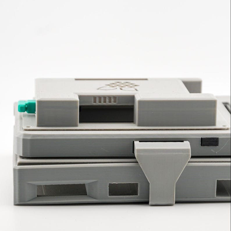 May include: A gray 3D printed case with a small green button and a slot for a micro SD card. The case has a logo of a raspberry with leaves on the top.