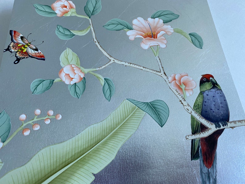 May include: A decorative panel with a silver background featuring a painted floral and fauna design. The artwork includes peach-colored flowers, green leaves, a colorful butterfly, and a bird perched on a branch. The overall aesthetic is elegant and nature-inspired.